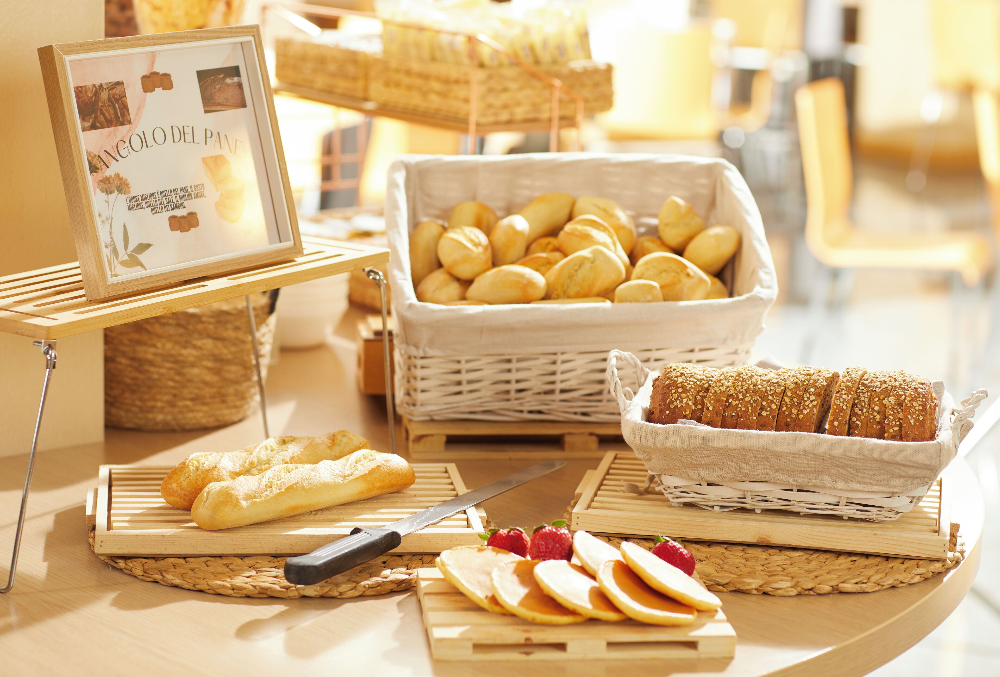 Un bufé de desayuno con panes, bollería y rebanadas de pan sobre tablas de madera.