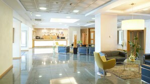 Un hall d’hôtel comprenant un comptoir d’accueil, des espaces de détente et une grande plante.