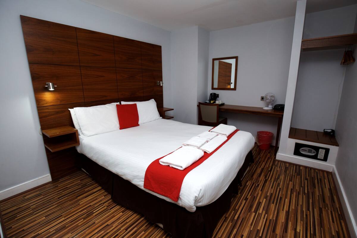 A modern hotel room with a large bed, wooden headboard, a desk, and a mirror.