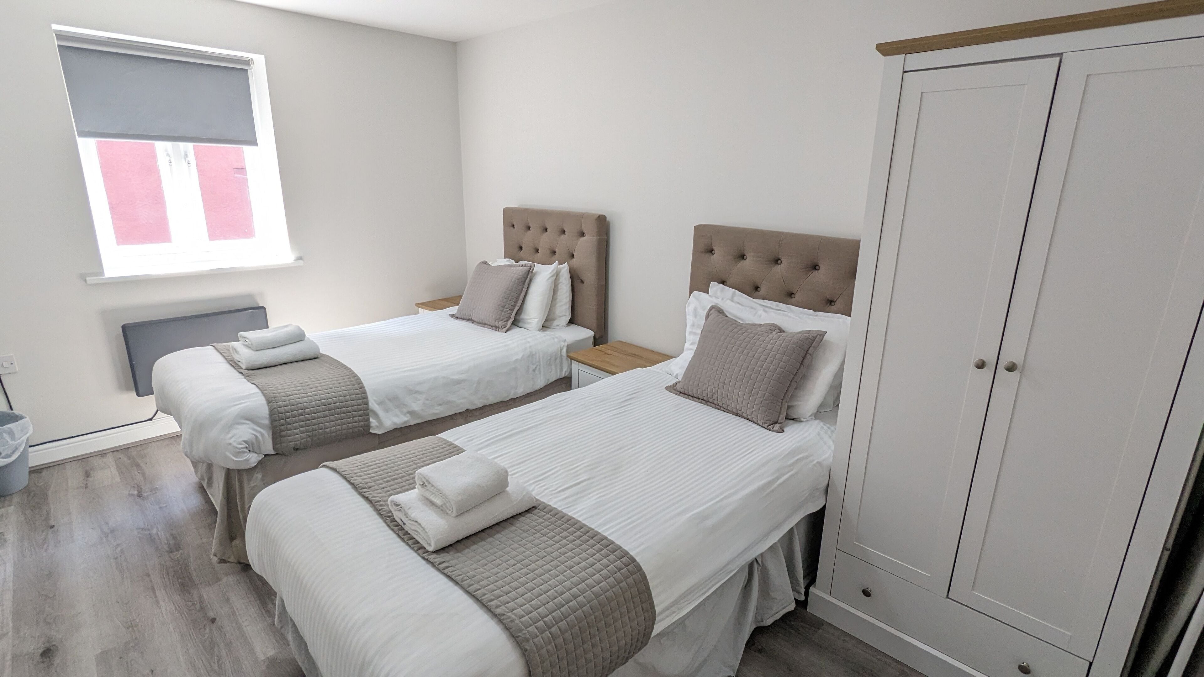 A hotel room with two beds, a wardrobe, and a window with blinds.