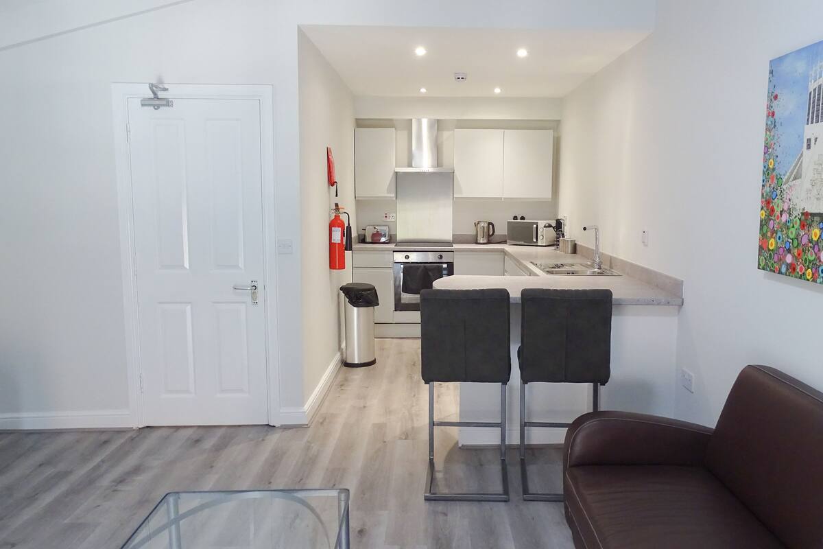 A modern kitchen with white cabinets, a stainless steel range, and a sink. There is a painting on the wall and a fire extinguisher mounted on the wall.