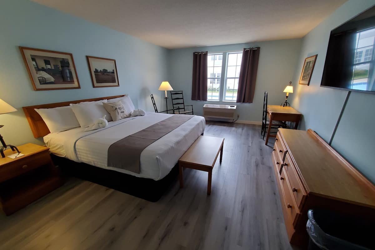 A hotel room with a bed, bedside tables, a desk, a chair, a TV, and a window with curtains.