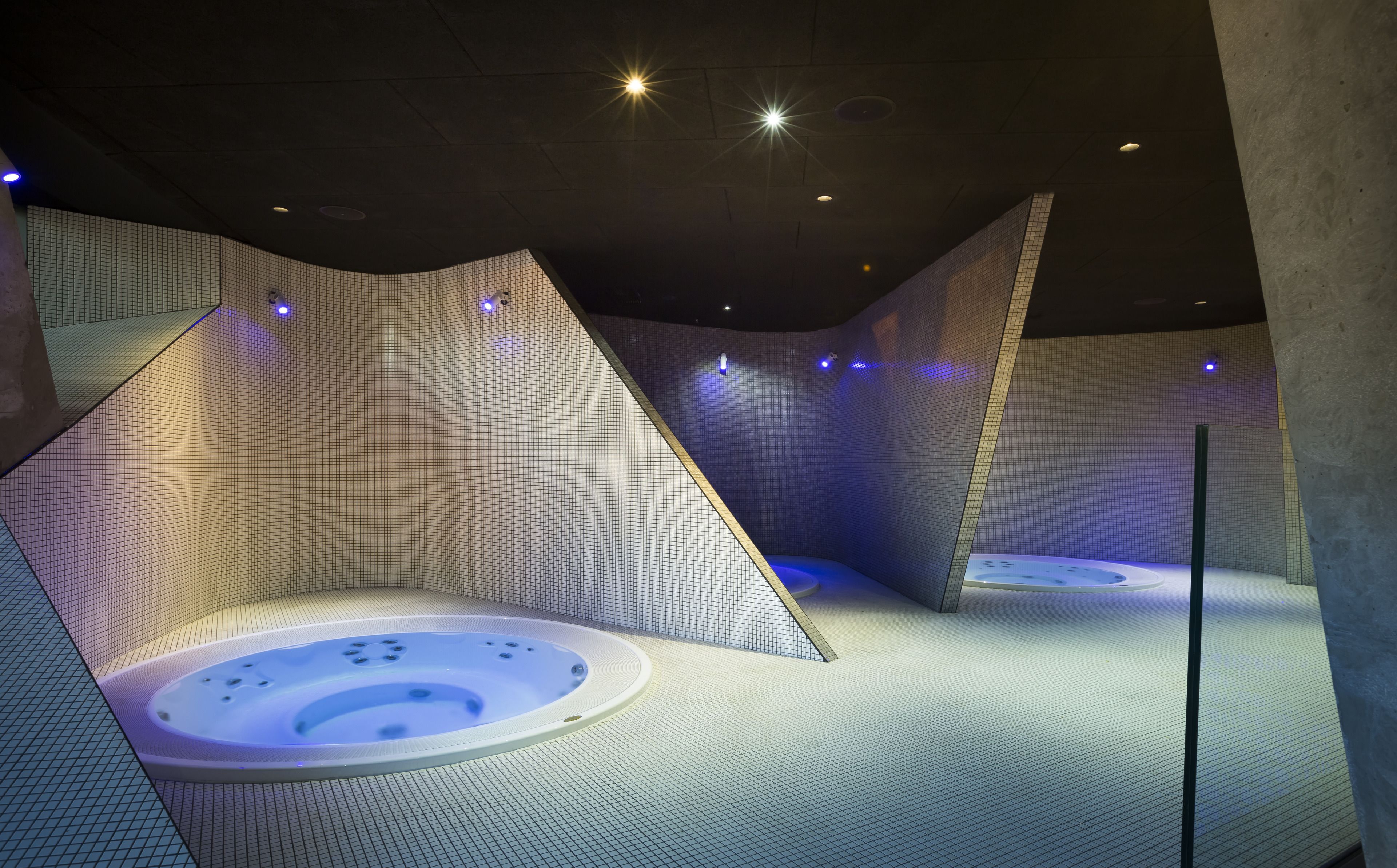 A modern spa room with a central hot tub, geometric wall designs, and ambient lighting.