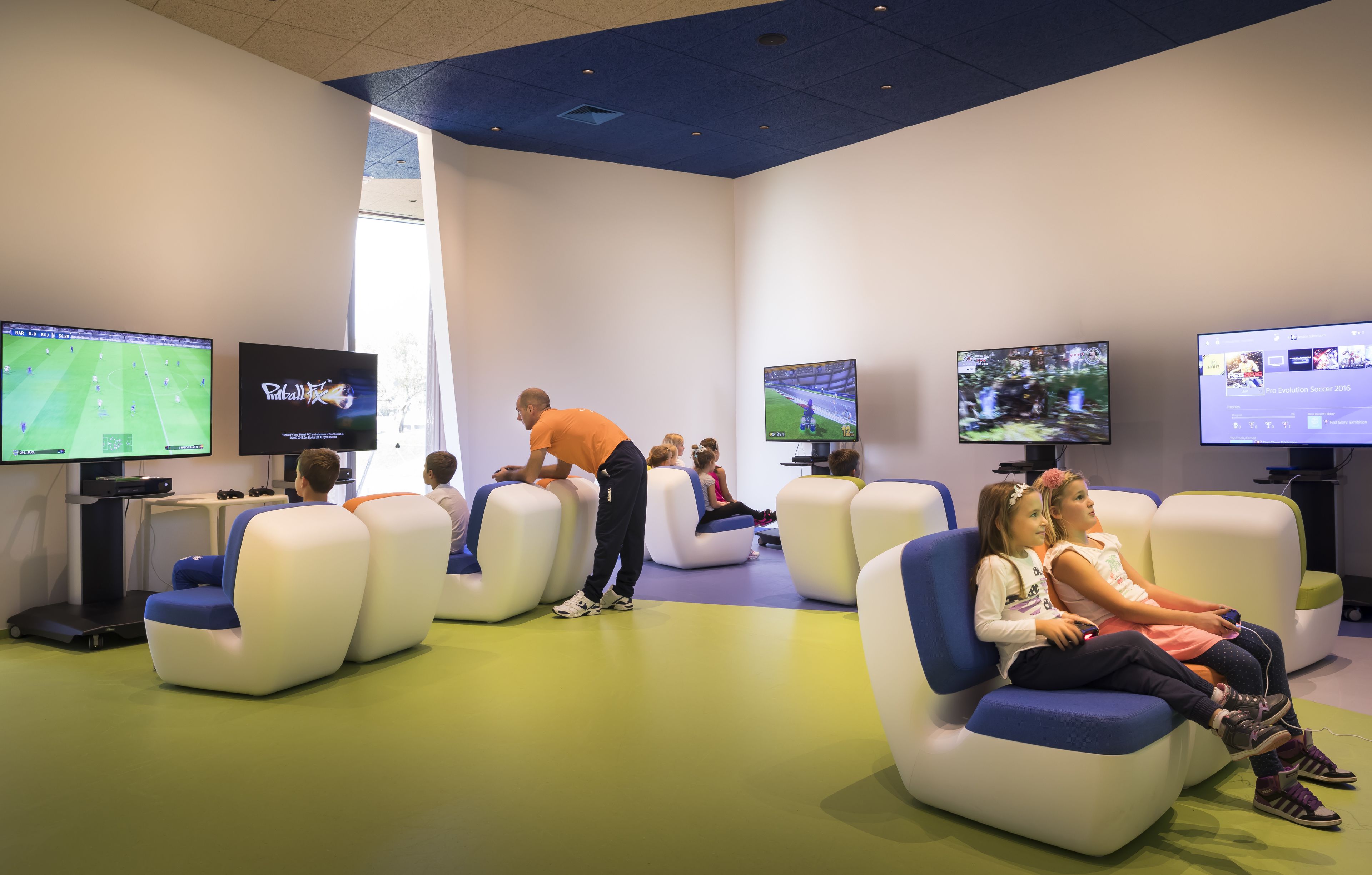 A modern lounge area with comfortable seating, multiple screens displaying sports content, and a bright, welcoming atmosphere.
