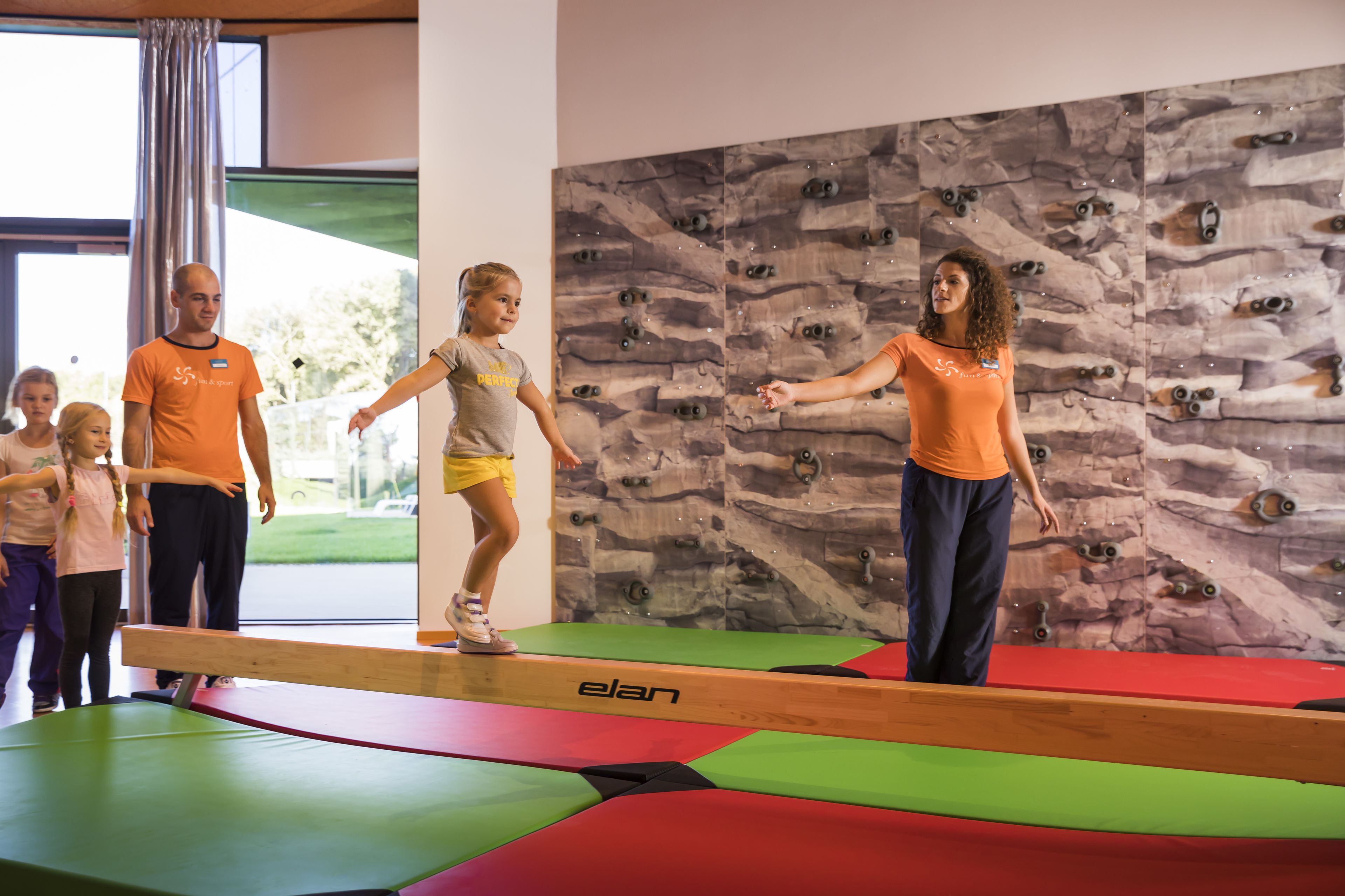 A climbing wall with a wooden handrail and padded mats.