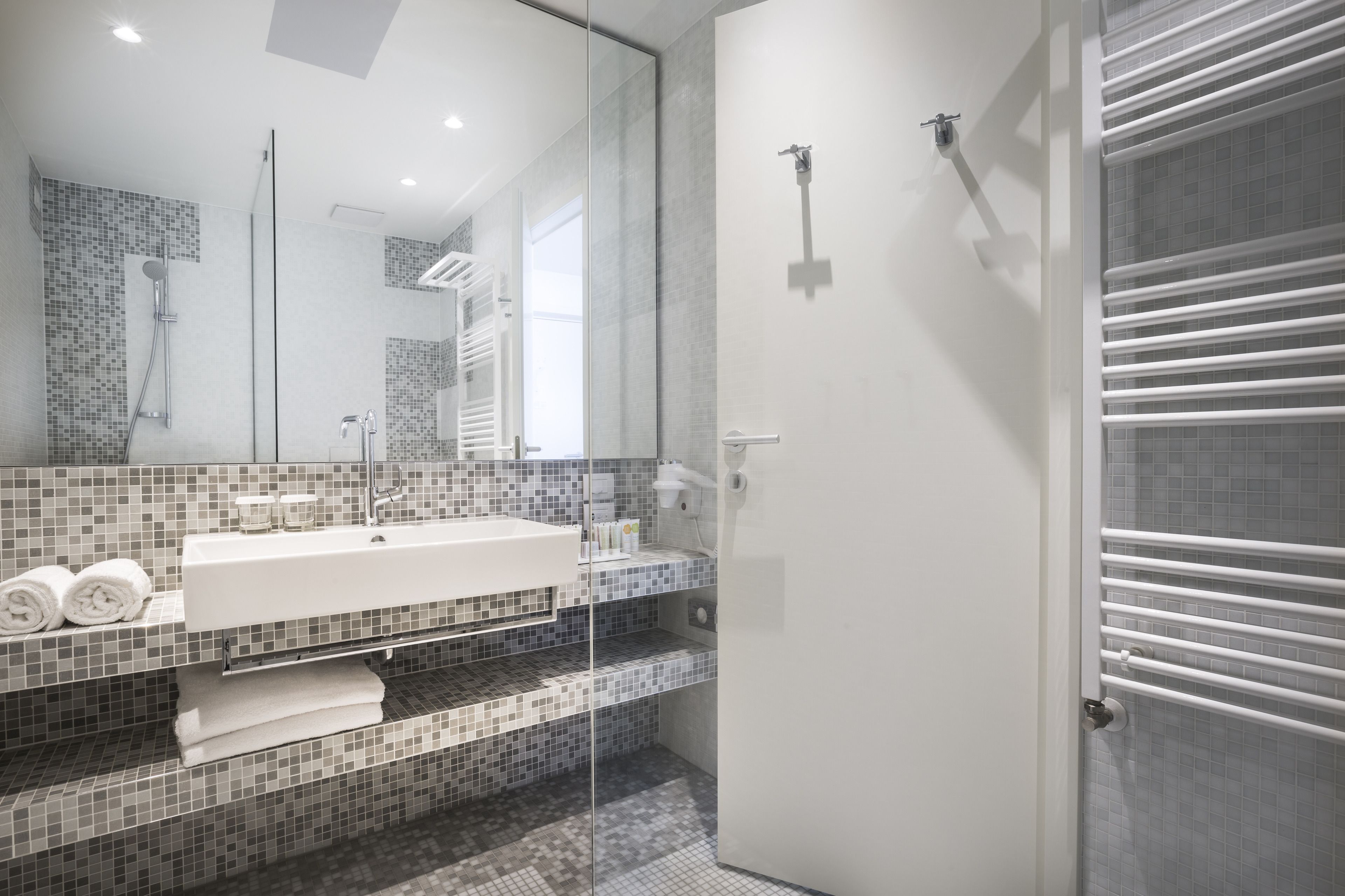 Um banheiro moderno com box de vidro, pia branca e painel de azulejos.