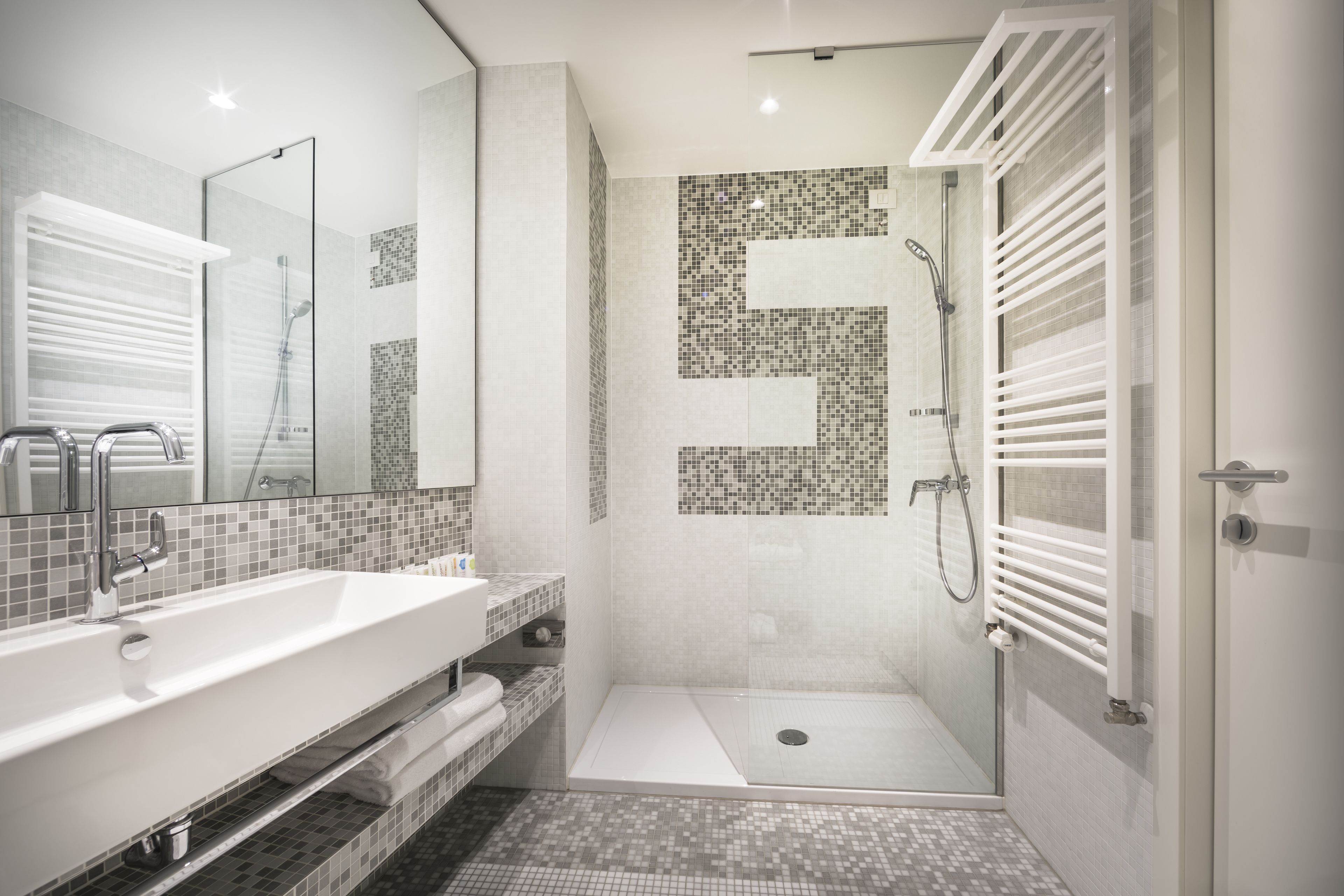 Un baño moderno con un lavamanos grande de color blanco, una cabina de ducha de cristal y un revestimiento de azulejos en la pared de la ducha.