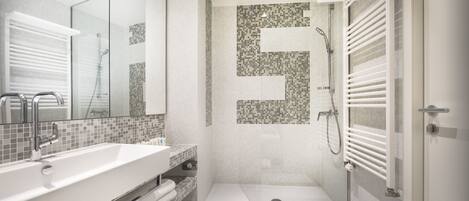 Un baño moderno con un lavamanos grande de color blanco, una cabina de ducha de cristal y un revestimiento de azulejos en la pared de la ducha.