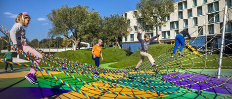Un terrain de jeux avec des équipements colorés et un bâtiment en arrière-plan.