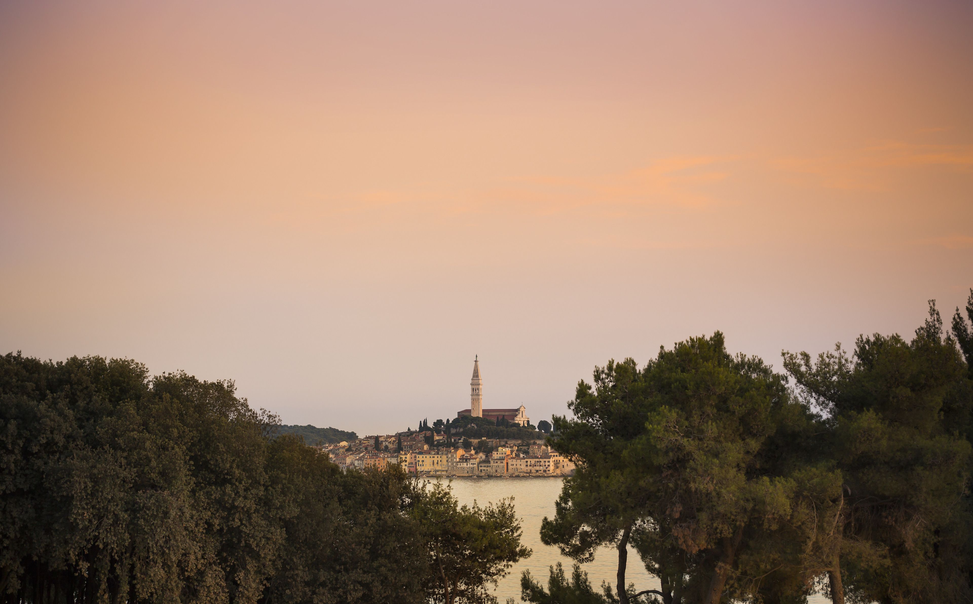 A coastal town with a prominent tower, surrounded by dense trees and a body of water.