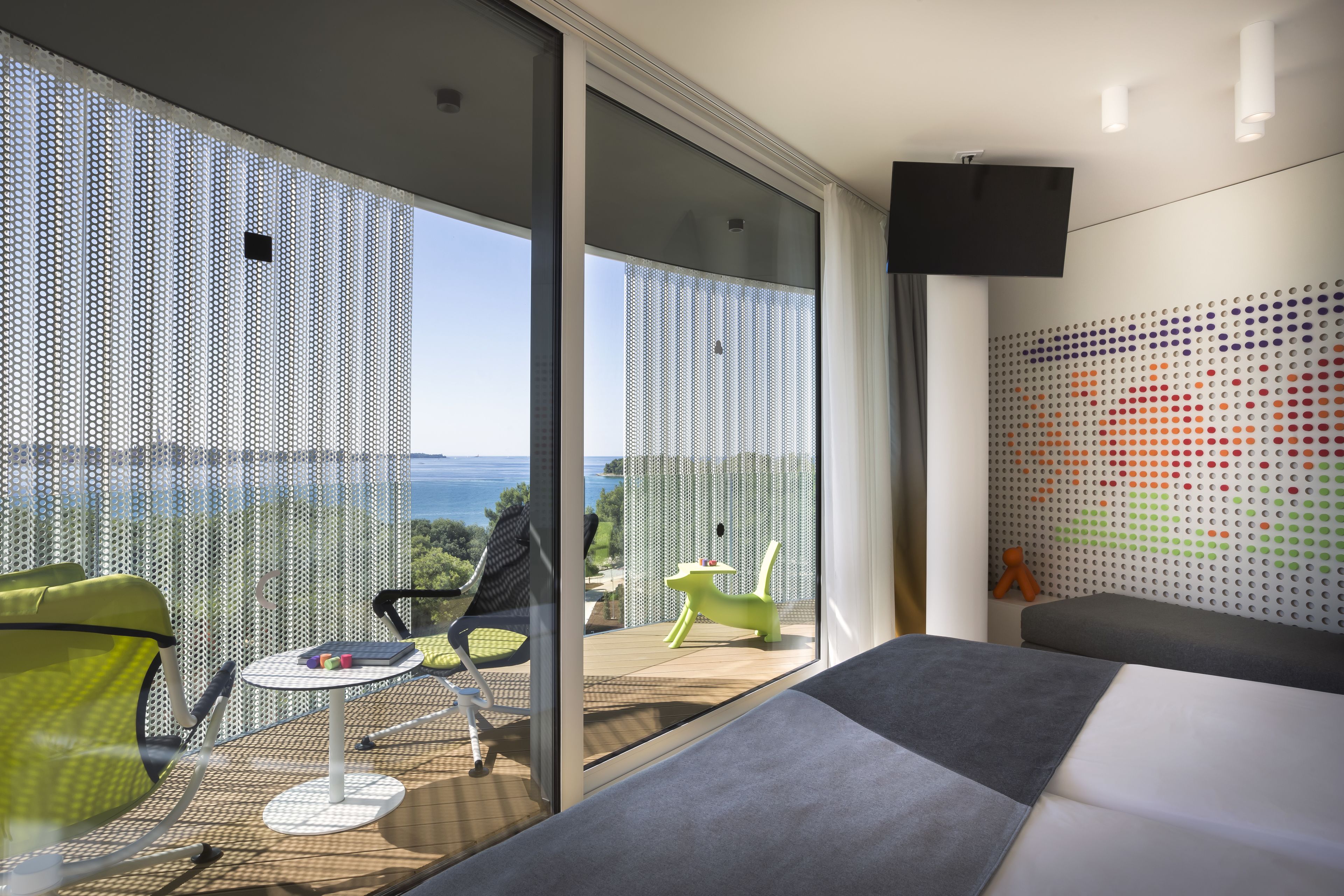 Habitación de hotel moderna con balcón, sofá, una mesita y pared con un patrón de puntos coloridos.