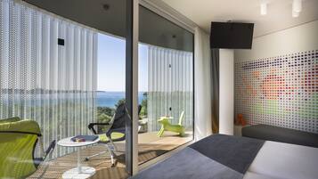 Habitación de hotel moderna con balcón, sofá, una mesita y pared con un patrón de puntos coloridos.