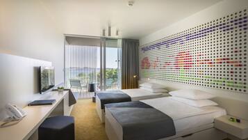 A modern hotel room with a desk, two beds, a large window, and a colorful dot-patterned wall.