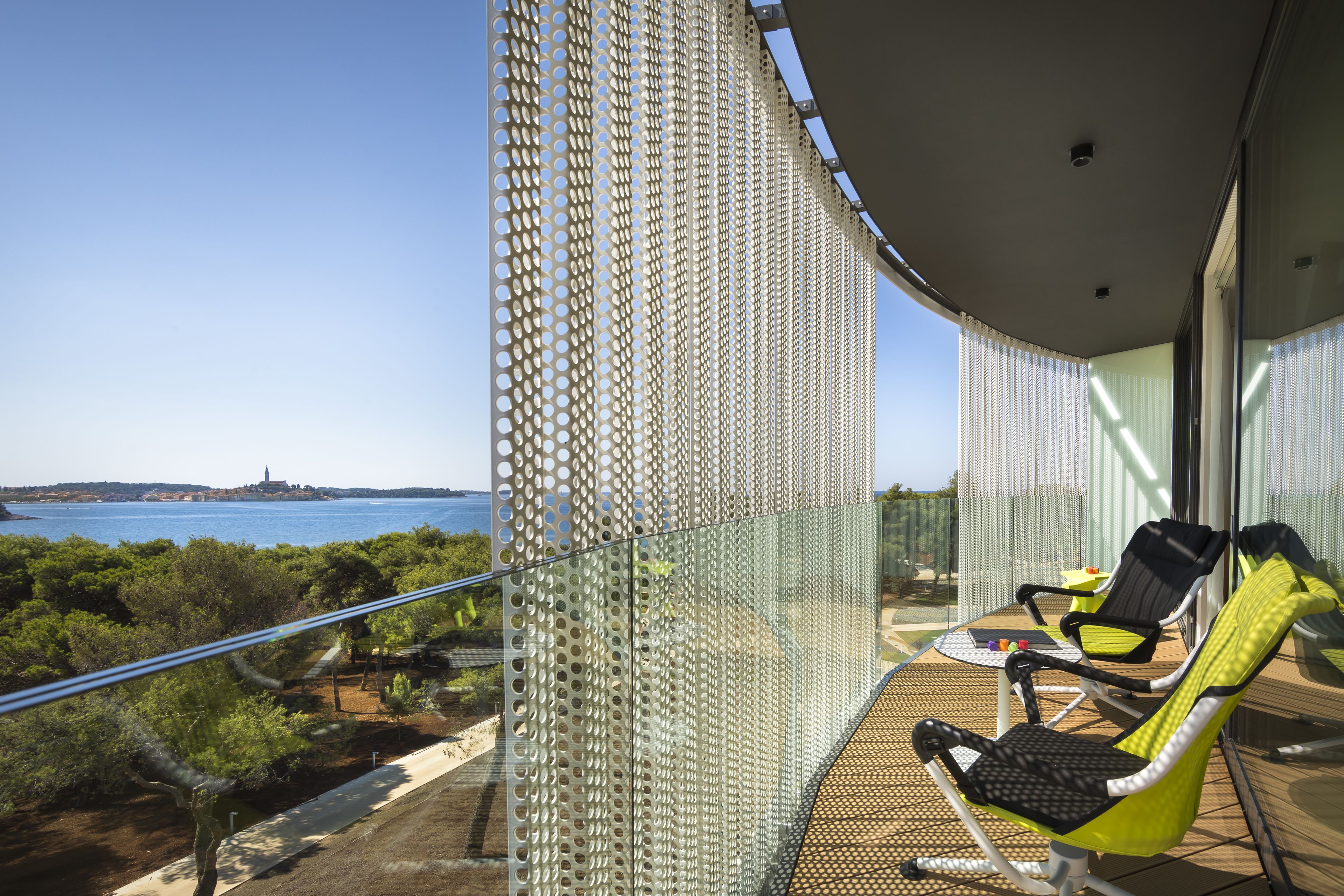 A balcony with two chairs, a table, and a view of the sea and distant land.
