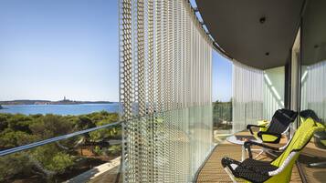 A balcony with two chairs, a table, and a view of the sea and distant land.