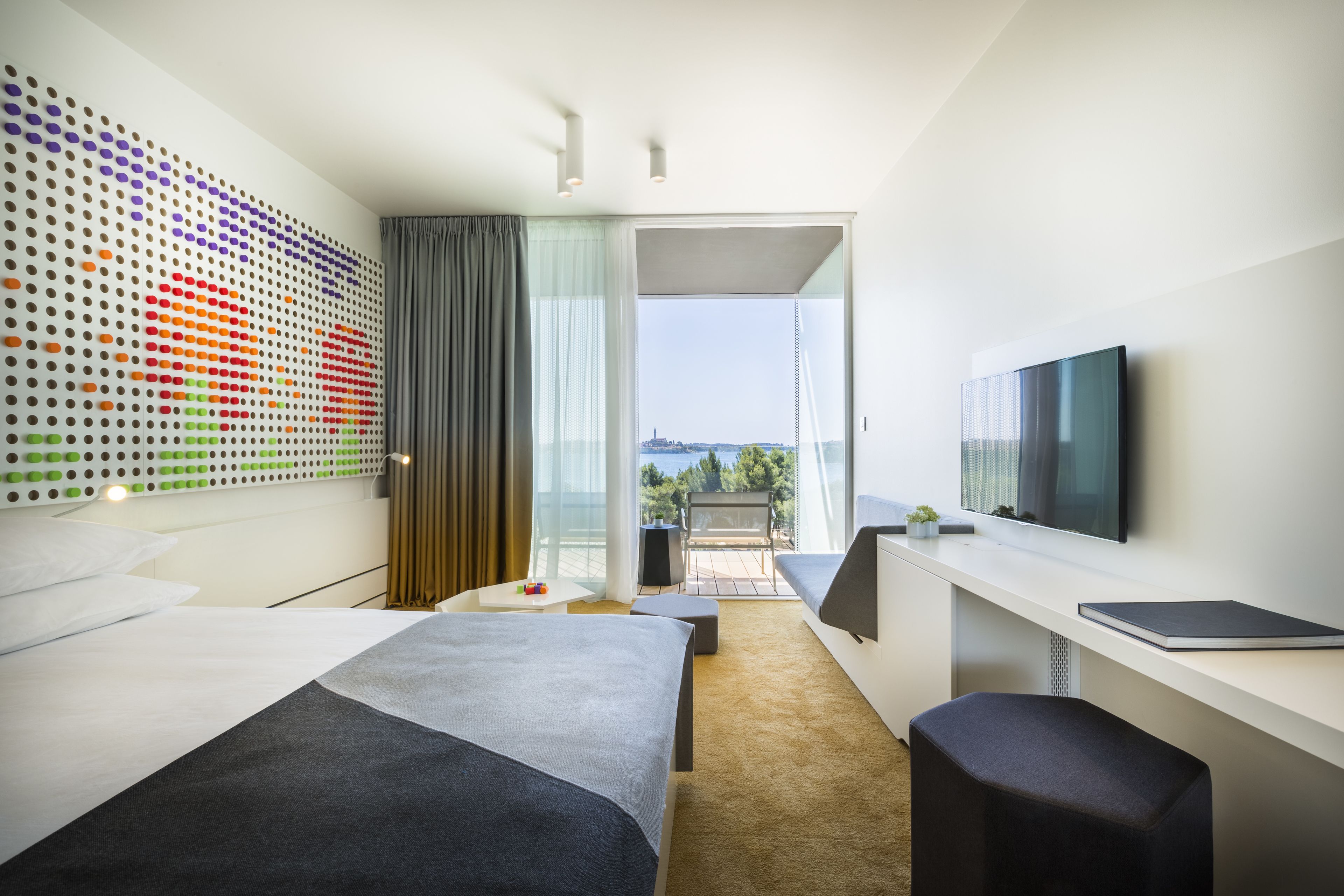 Habitación de hotel moderna con una cama grande, un escritorio, un televisor de pantalla plana y un balcón con vistas a la ciudad.