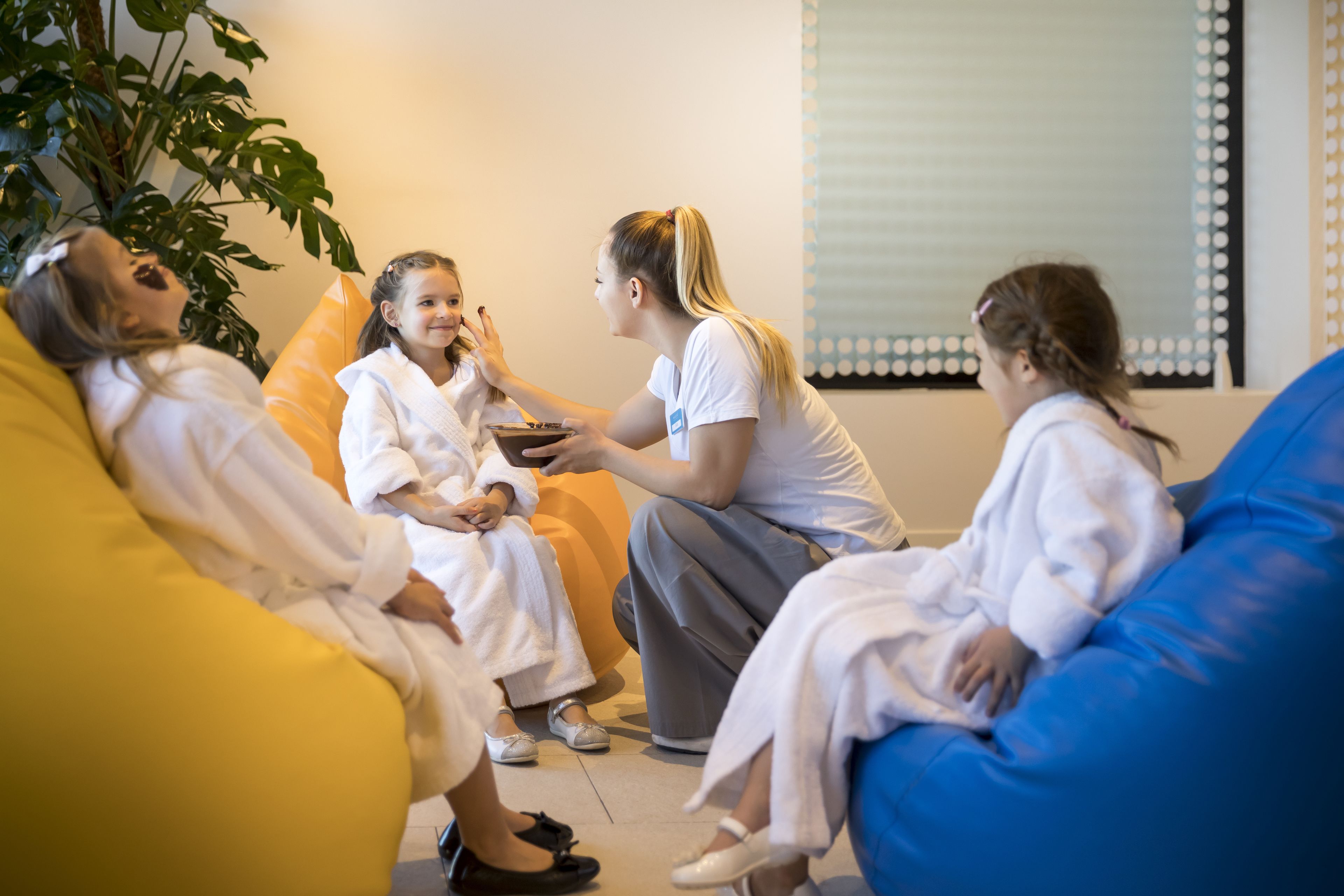 A group of people sitting on bean bags in a room with a large plant and a window with blinds.
