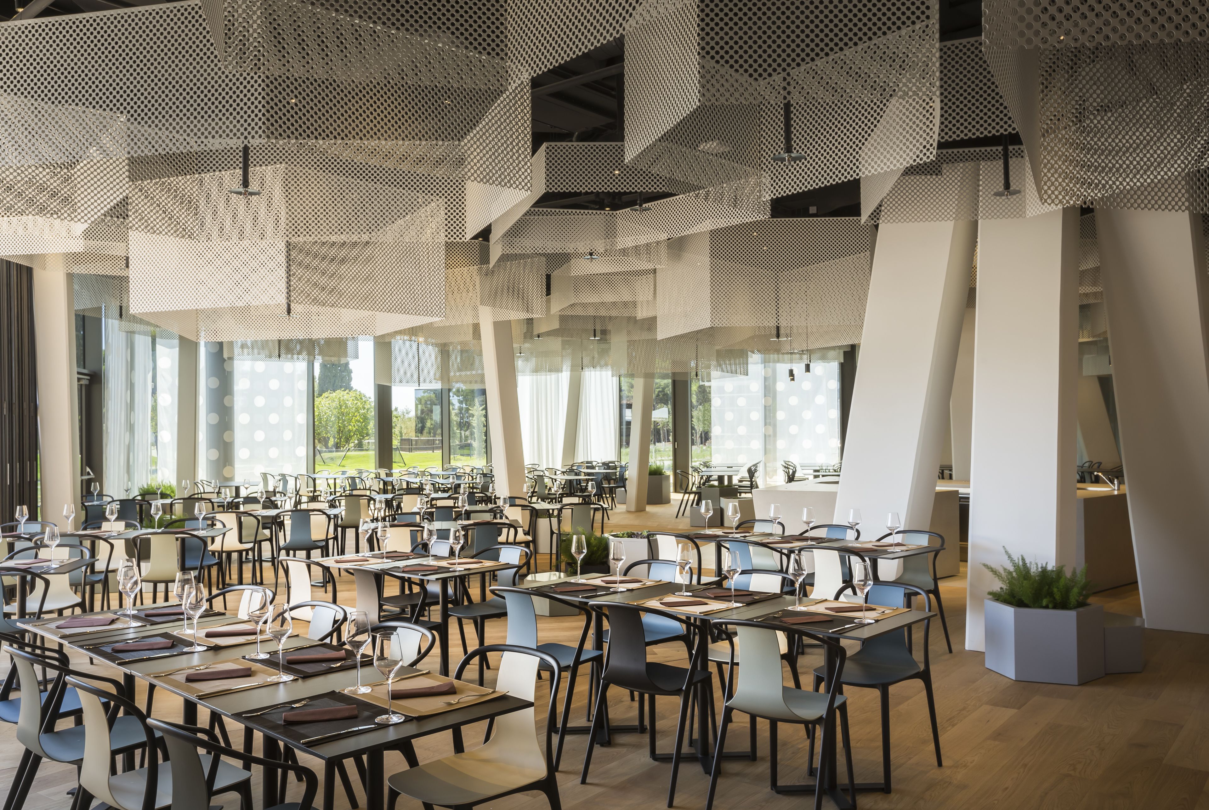 Un vaste espace dédié à la salle à manger, avec de nombreuses tables et chaises, de grandes fenêtres et un design moderne au niveau du plafond.