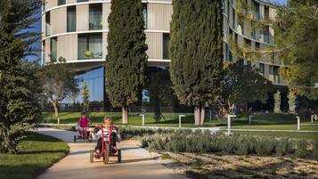 Un edificio moderno con fachada curva, rodeado de jardines cuidados y árboles altos.