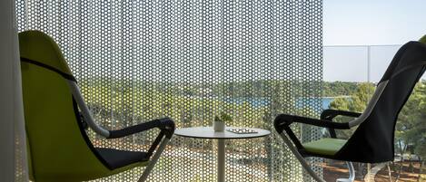 A balcony with two chairs and a small table, a perforated screen, and a view of greenery and buildings.
