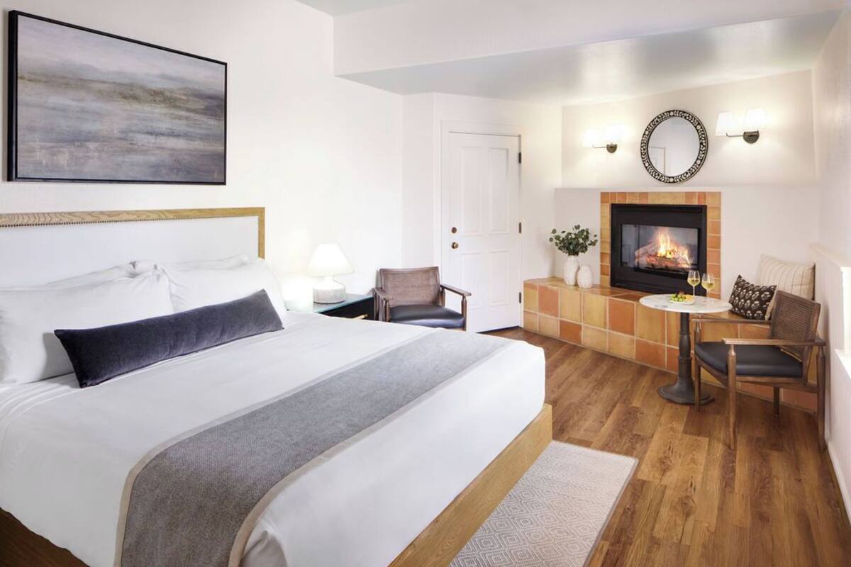 Una habitación de hotel con cama, chimenea, zona de estar con mesa y sillas, y una puerta.