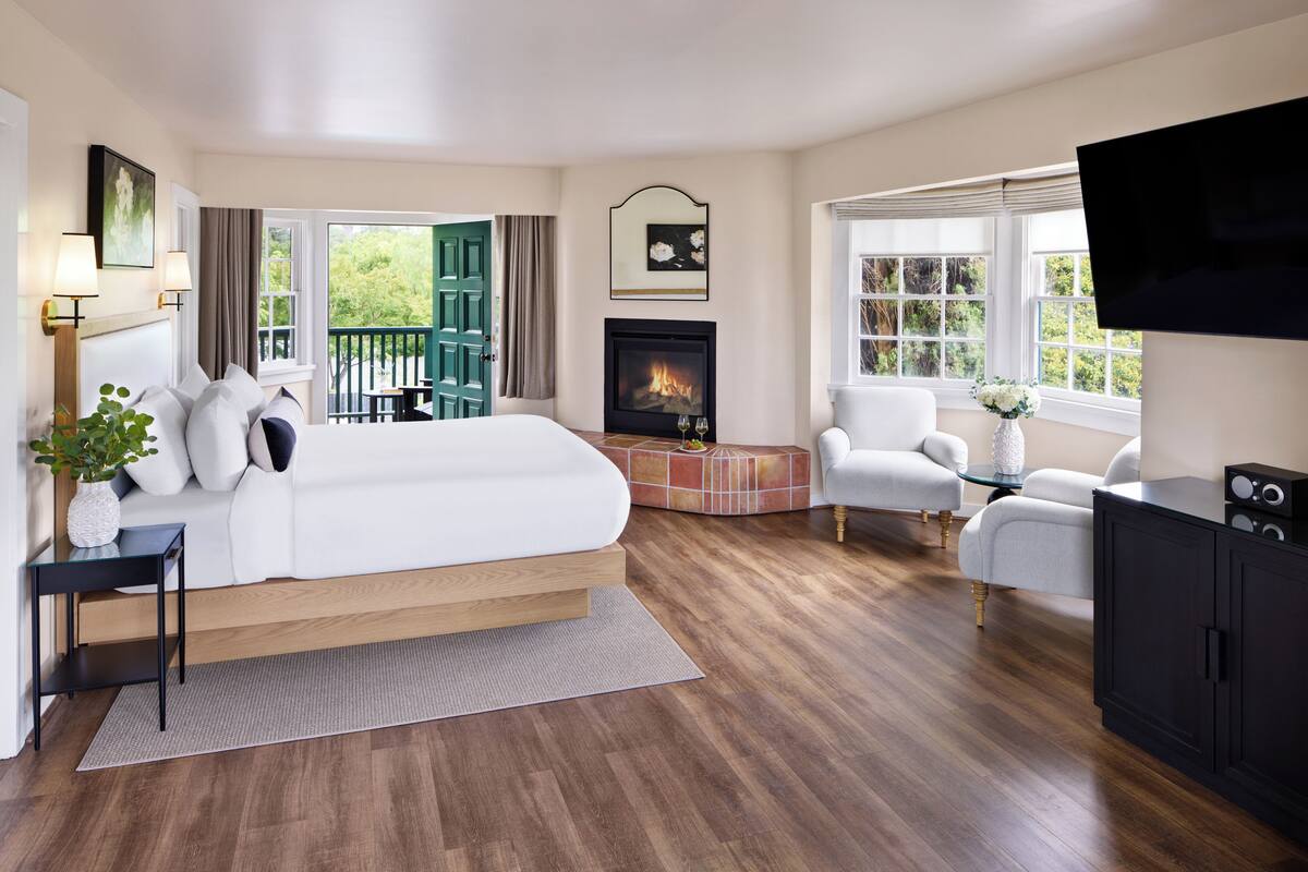 Habitación de hotel moderna con una cama grande, una chimenea, un televisor y un balcón con una puerta verde.