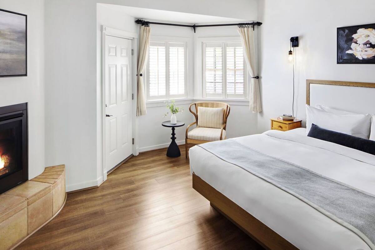 Un dormitorio con una cama grande, una silla, una mesita y una chimenea.