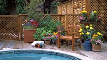 A wooden deck with a pool, surrounded by potted plants and a wooden chair.