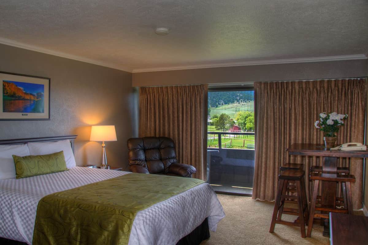 Ein Hotelzimmer mit einem Bett, einem Sessel, einem Tisch mit Stühlen, einer Lampe, einem Bild an der Wand und Blick aus dem Fenster.