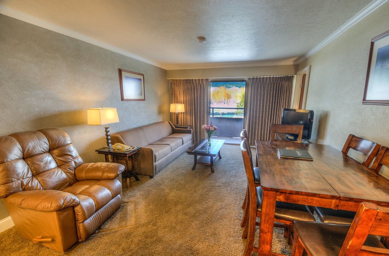 Habitación de hotel con sofá de cuero, una mesa de comedor de madera, una mesa de centro y un televisor.