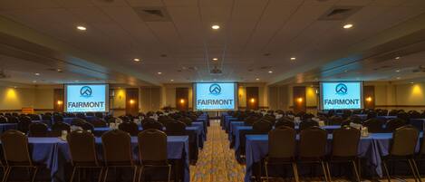 Een congreszaal in Fairmont Hot Springs Resort met rijen tafels en stoelen, een vloerbedekt met tapijt en een projectiescherm waarop de naam van het resort staat.