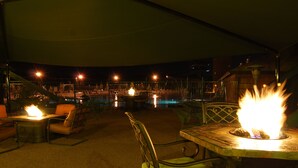 An outdoor seating area with tables and chairs, a fire feature, and a view of the marina in the background. - Fairmont Hot Springs Resort (Anaconda)
