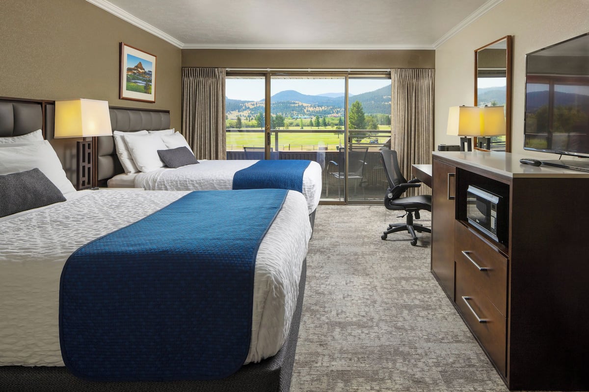 Ein Hotelzimmer mit zwei Betten, einem Schreibtisch mit Fernseher und einem Balkon mit Blick auf die Landschaft.