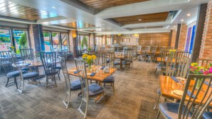A spacious restaurant with multiple tables and chairs, large windows, and a brick wall. - Fairmont Hot Springs Resort (Anaconda)
