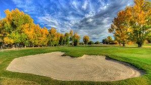 A golf course with a sand bunker, trees with autumn foliage, and a clear sky. - Fairmont Hot Springs Resort (Anaconda)