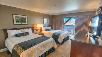 A hotel room with two beds, a desk, a television, and a window with curtains.