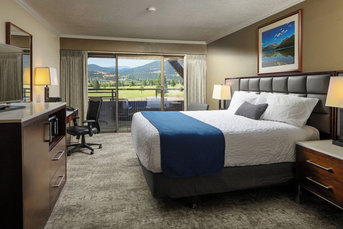 Ein Hotelzimmer mit einem großen Bett, einem Schreibtisch mit Computer, einem Sessel und Blick auf eine Berglandschaft durch das Fenster.