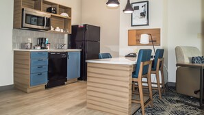 Eine moderne Küche mit Mikrowelle, Kühlschrank und Geschirrspüler. Ein Essbereich mit blauen Stühlen und einem kleinen Tisch ist ebenfalls vorhanden.