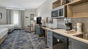 A hotel room with a bed, desk, kitchenette, and a television. - Candlewood Suites Longview by IHG (Longview)