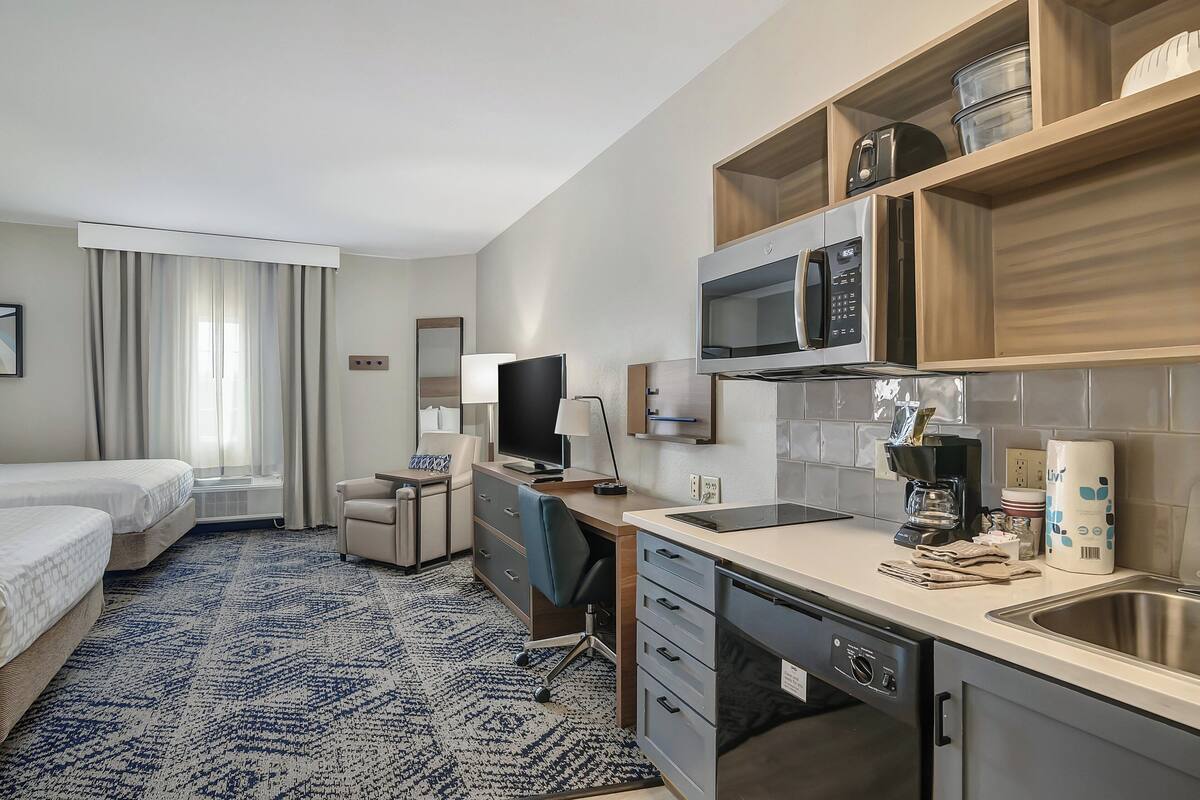 A hotel room with a bed, desk, kitchenette, and a television.