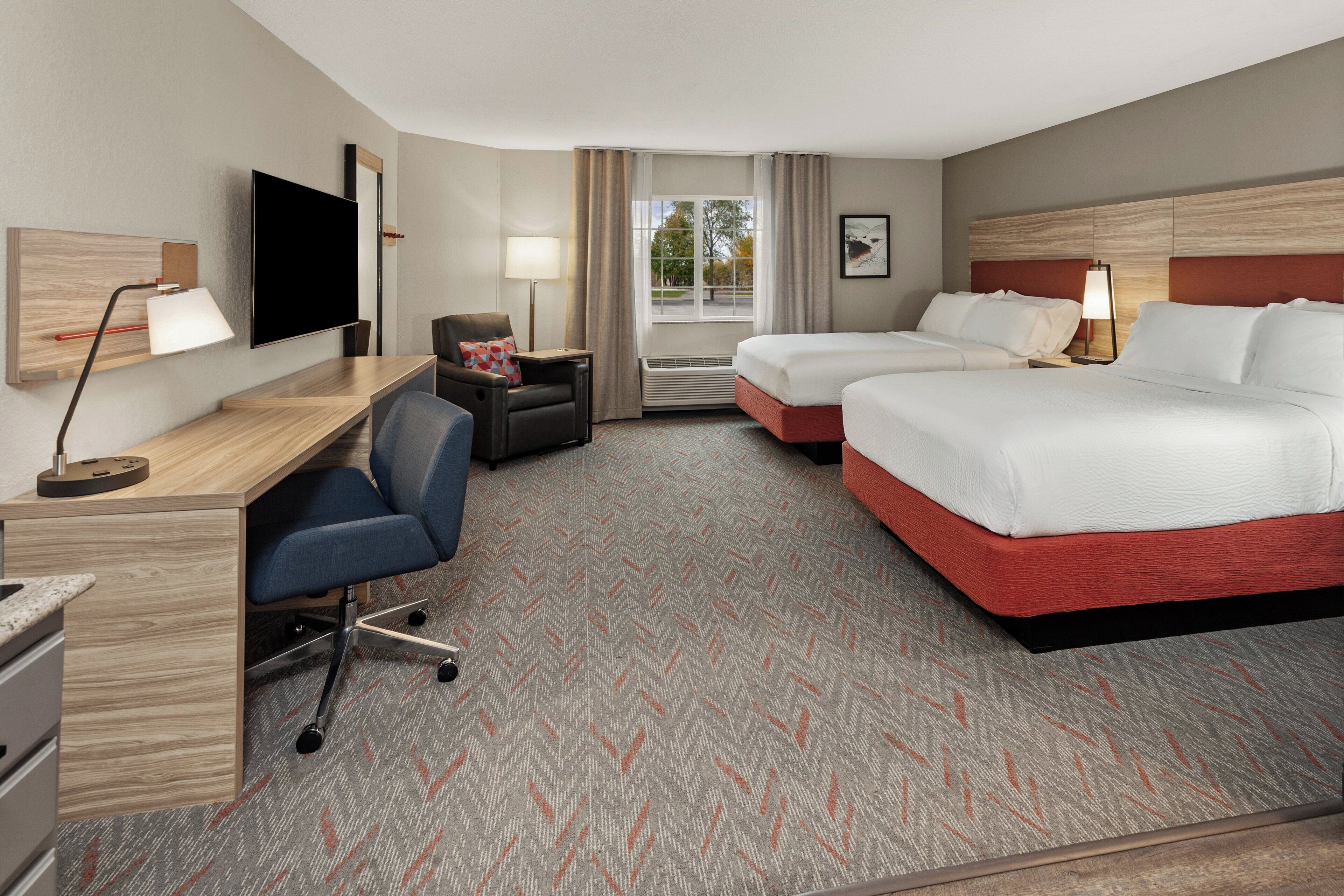 A hotel room with a desk, two beds, a TV, and a window with curtains.