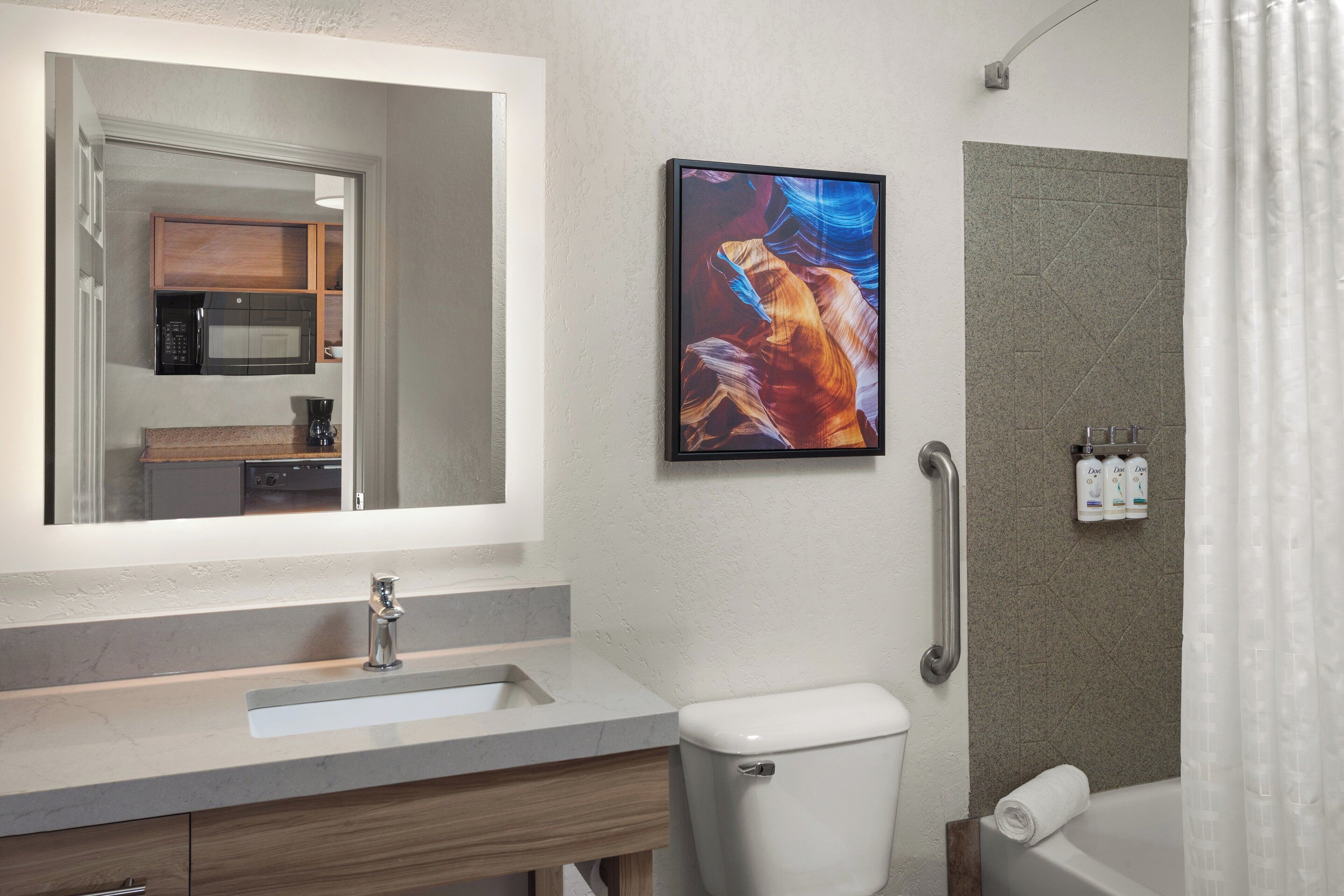 A bathroom with a sink, toilet, shower, and a framed picture on the wall.