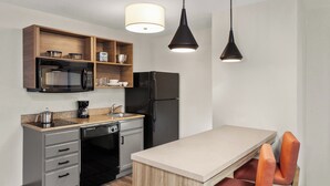 A compact kitchen with a microwave, refrigerator, and wooden shelves. There are two pendant lights above the counter.