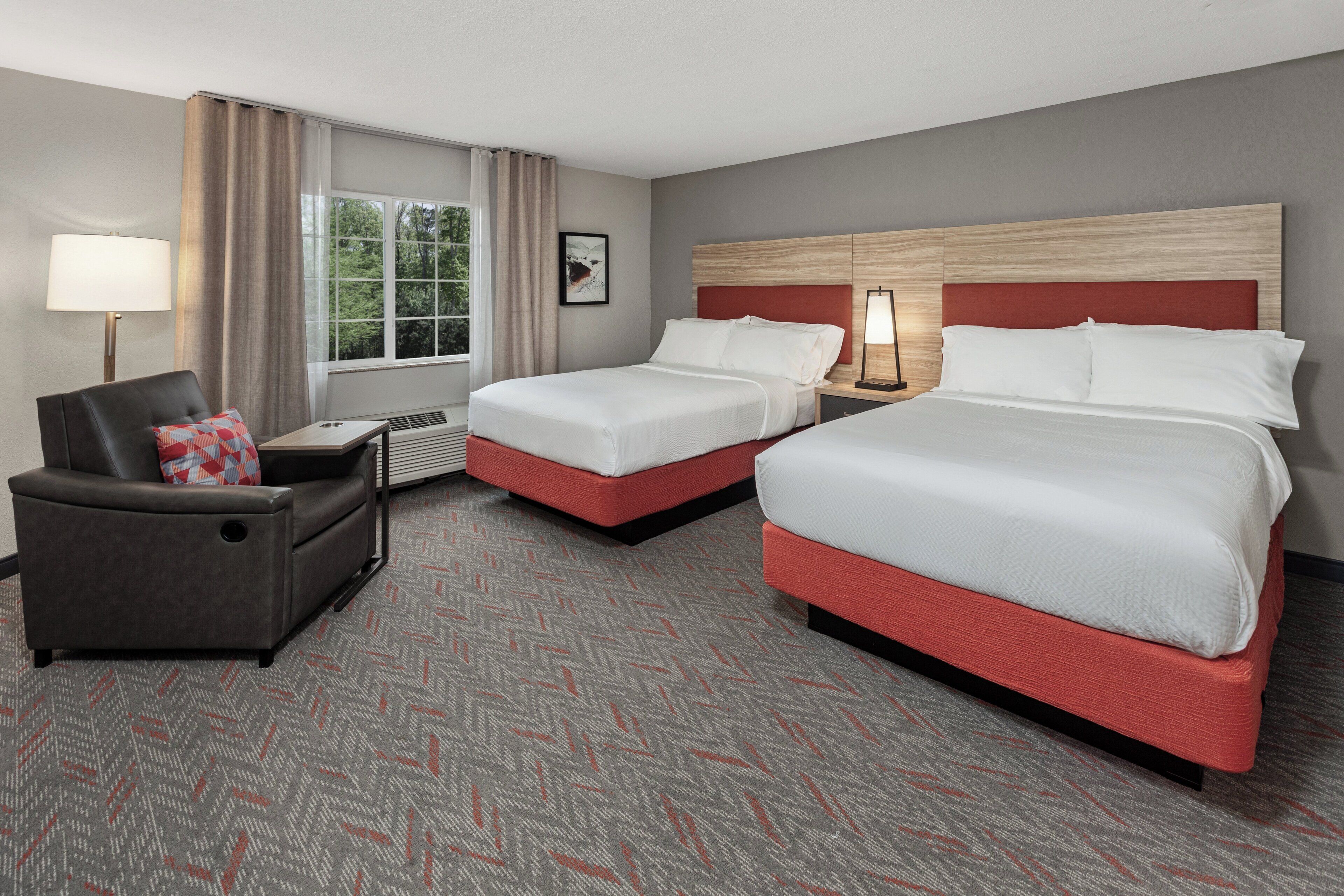 A hotel room with two beds, a sofa, a desk, and a window with curtains.