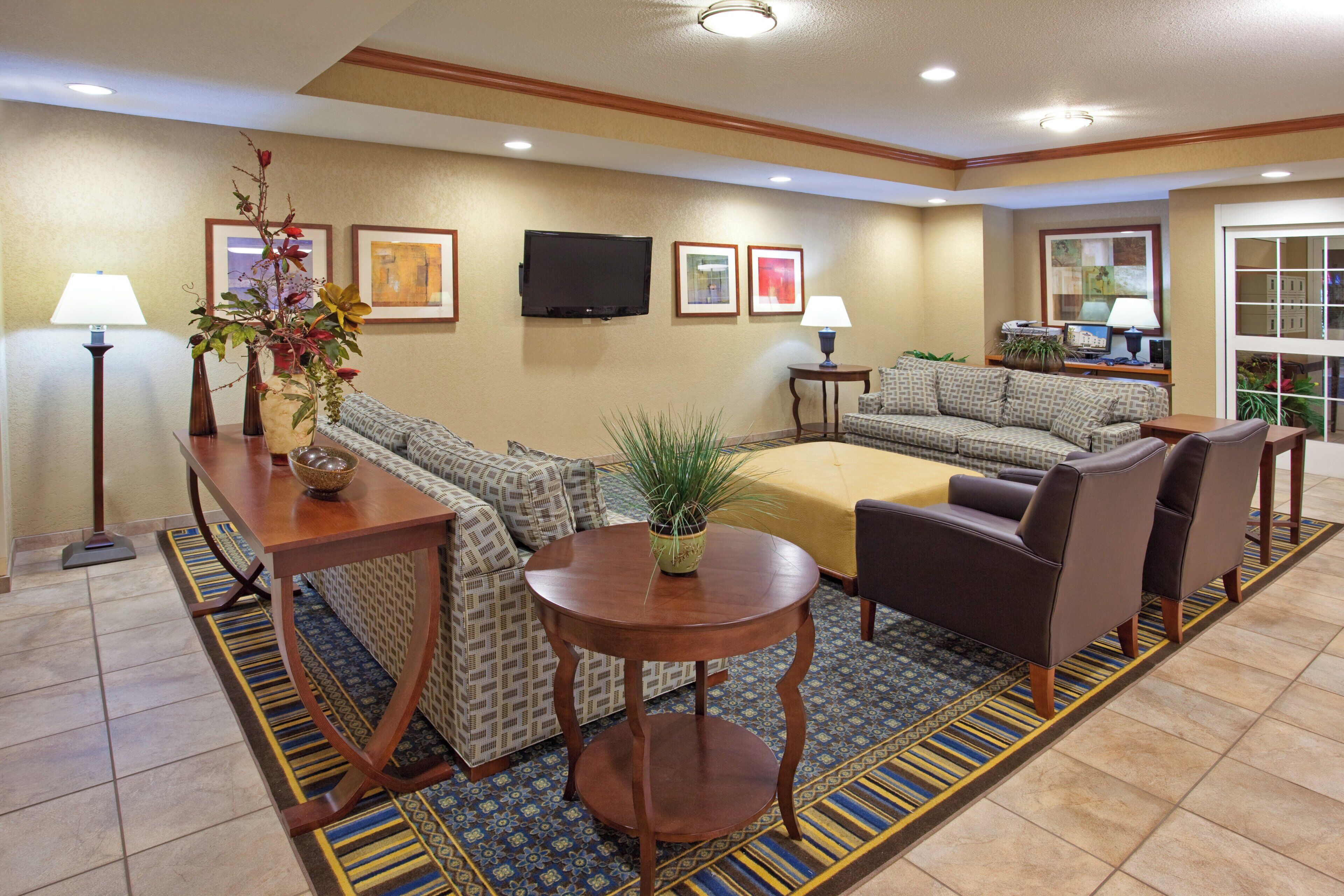 A hotel lobby with a sofa, chairs, a table, a TV, and artwork on the walls.