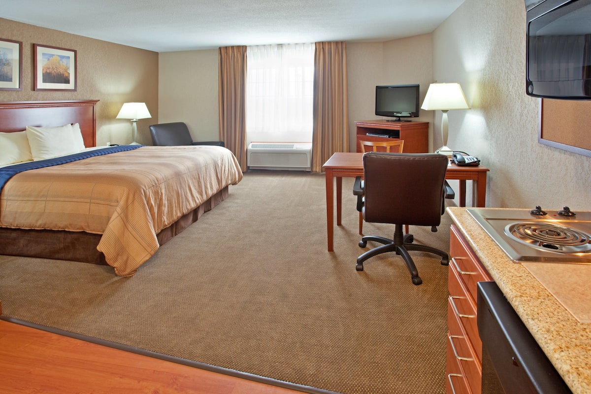 A hotel room with a bed, a desk, a chair, a television, and a kitchenette.