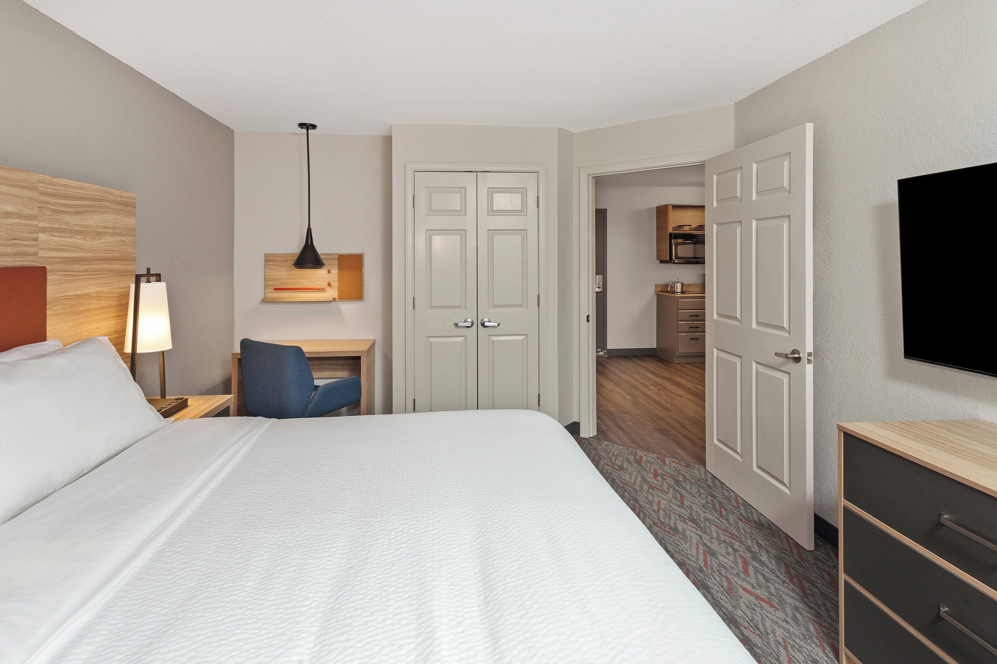 A hotel room with a large bed, a desk with a chair, a TV, and a wardrobe.