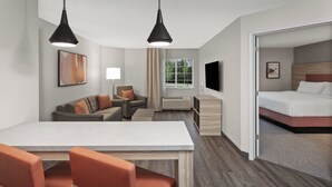 A hotel room with a dining area, a sofa, a TV, and a bed.