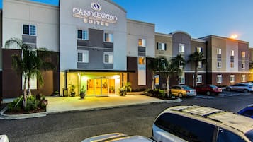 A hotel with a modern facade, multiple entry points, and a parking lot with several cars.