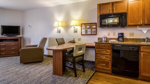 A compact hotel room with a kitchenette, a dining area with a table and chairs, a flat-screen TV, and a small sofa. - Candlewood Suites Jacksonville East Merril Road by IHG (Jacksonville)